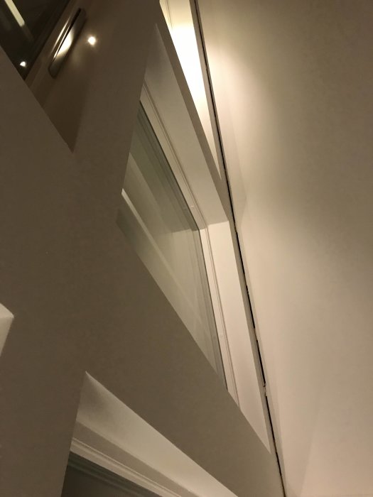 Vinkelvy av en dåligt målad dörrkarm och vägg som reflekterar ljus, indikerande målningsfel vid entrén.