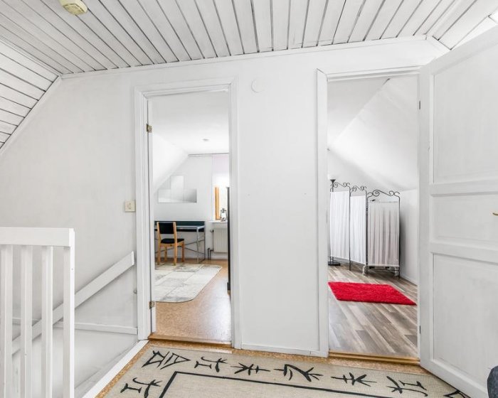 Interiör av ett hem med öppen dörr som leder till ett rum med stora radiatorer under fönstren.