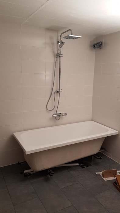 Badkar utan sidor monterat i hörn med uppsatt handdukstork och dusch ovanför, i ett badrum under renovering.