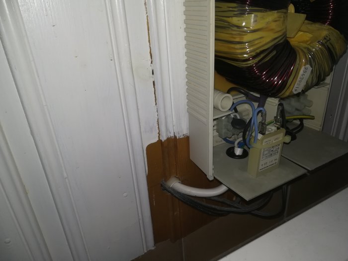 Transformator för golvvärme, ojordad, med kablar och installation i hörn vid vitmålad vägg.