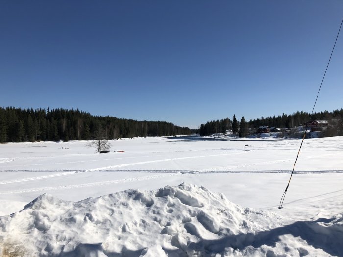 Vintervy över frusen Västerdalälven med snötäckt landskap och skog i bakgrunden.