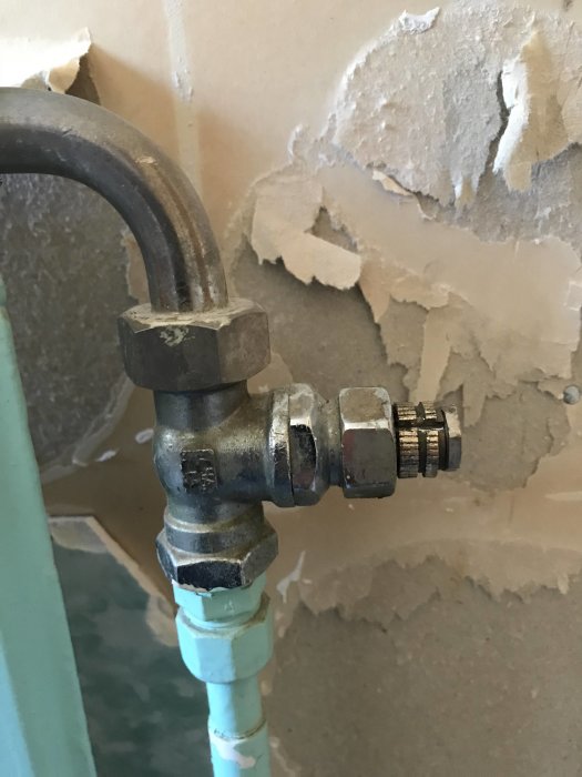 Radiatoranslutning med avstängningsventil mot sliten vägg, redo för demontering.