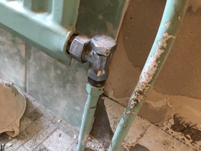 Radiatorkoppling med avstängningsventil vid en vägg med delvis borttaget kakel.