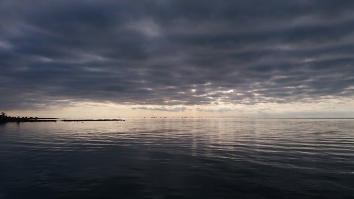 Mörka moln över en stilla havsyta med svaga ljusinslag i horisonten.