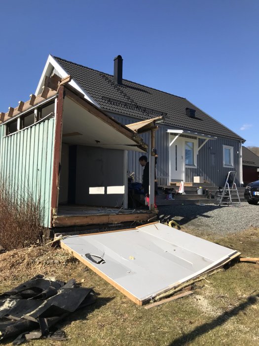 Rivning av gammalt förråd med spillror och byggavfall på gräsmattan framför hus.