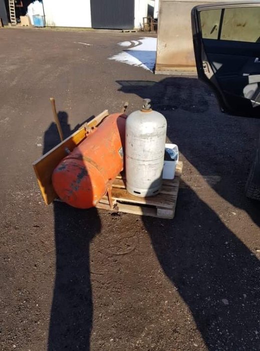 En orange och en vit gasflaska på en pall bredvid några verktyg utomhus.
