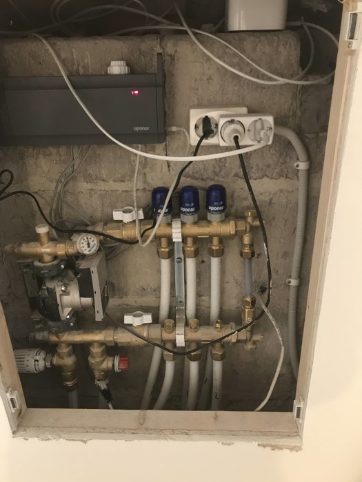 Öppet skåp med installation av golvvärmesystem inklusive rör, fördelare och kopplingar, vissa lock borttagna.