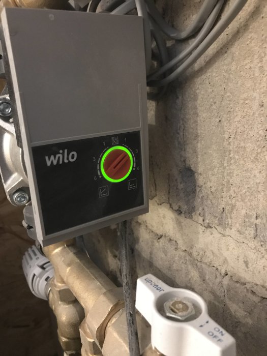 Värmesystemets cirkulationspump märkt 'wilo' med grönt inställd vred på cirka 3 och en vit avstängningsventil.