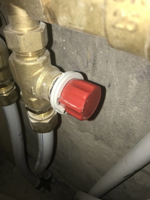 VVS-installation med en röd ventil mot en grå betongvägg och angränsande vita rör.