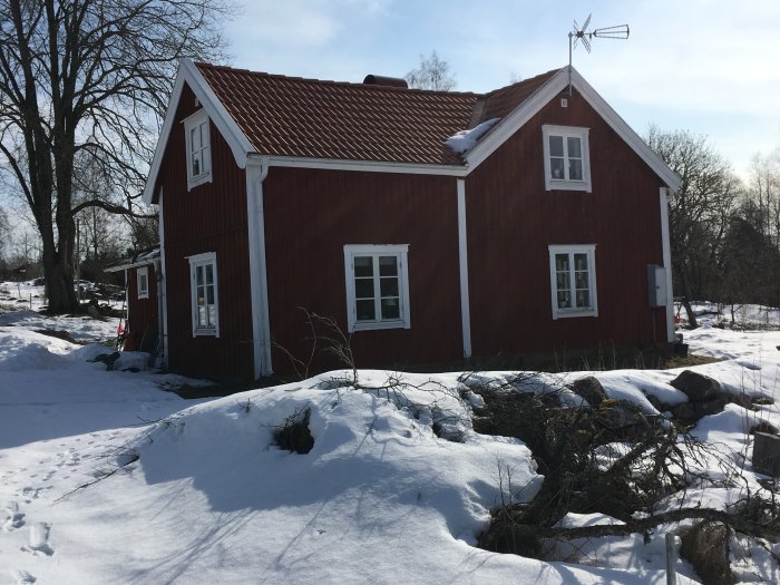 Röd trävilla med snöklädd mark, visar gavel och veranda för potentiell utbyggnad.