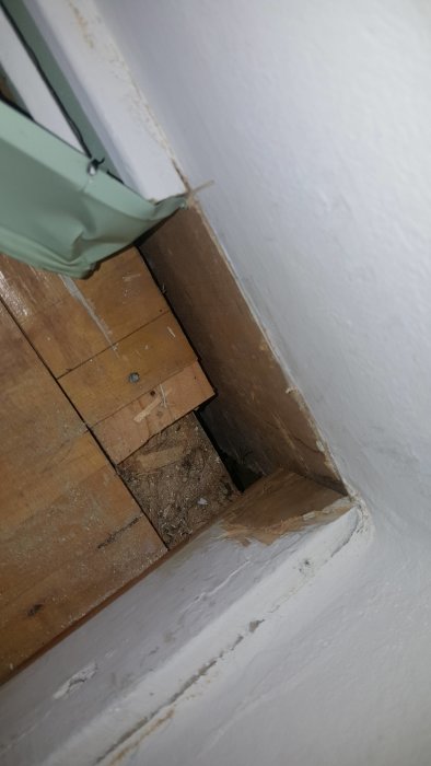 Öppen golvhörna där väntat värmesystem saknas, med synliga trägolvsplankor och en vitmålad vägg.