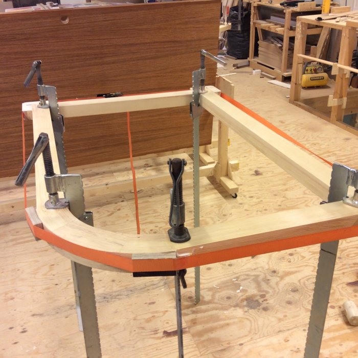 Träsnickeriprojekt med delar i skruvstäd och klämmor på arbetsbord i verkstad.