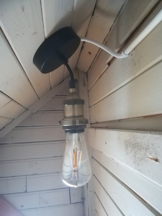 Nyinstallerad lampa med synliga glödtrådar på en vitmålad kattvind.