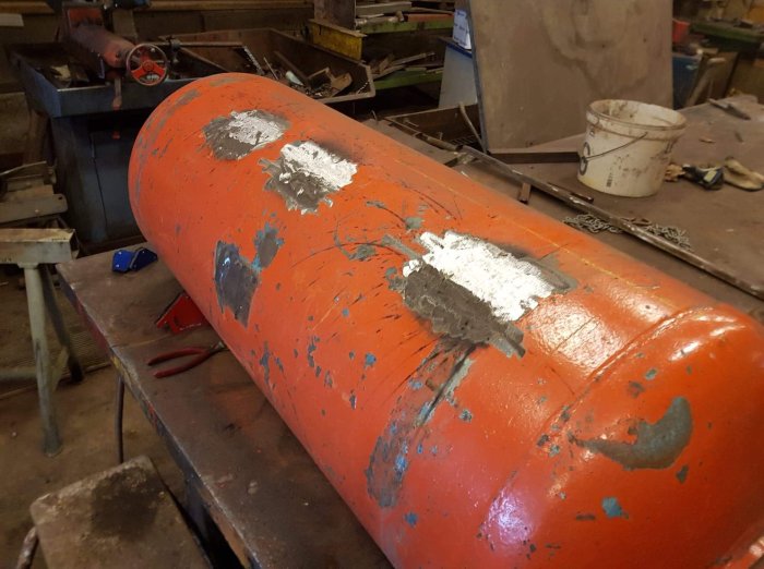 Svetsfogar på en orange cylinder i en verkstad, med slipade ytor efter svetsning.