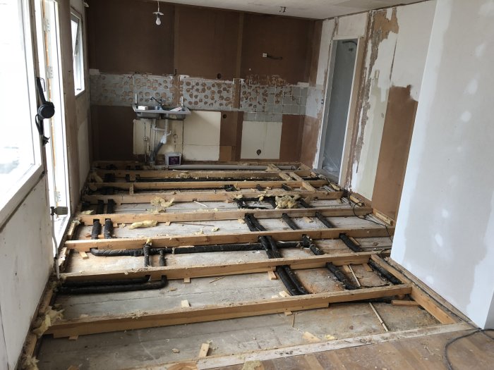 Köksrenovering med blottade avloppsrör och värmerör i ett hus från 1970, parkett golvet är borttaget.