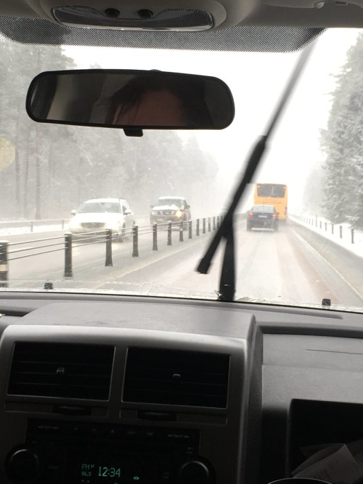 Snöig väg sett från bilens förarplats med fordon framför, mitt i snöfall.