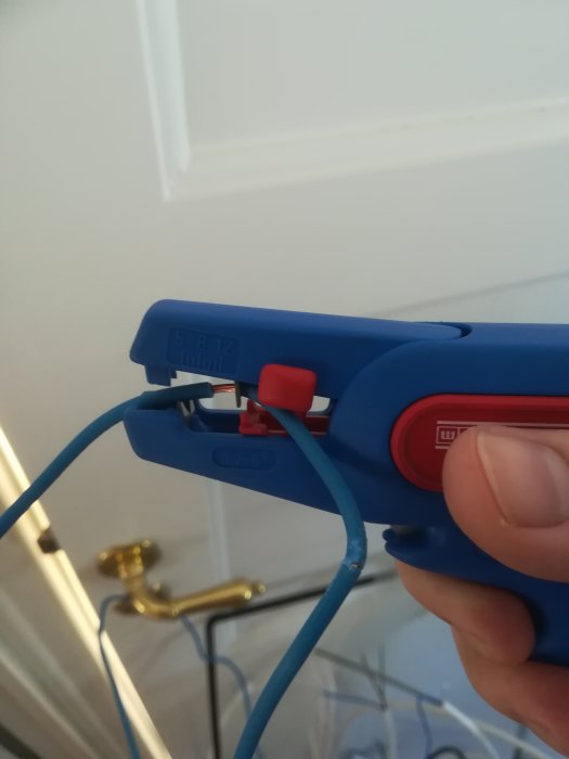 Hand som använder en blå skaltång för att vika en elektrisk kabel åt sidan.