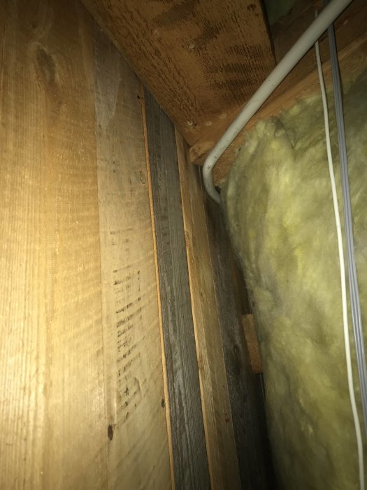 Tätt luftspalt mellan träreglar och isolering i en husvägg, med en synlig elkabel.
