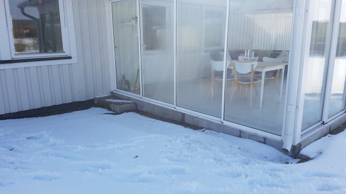 Uterum med skjutdörrar i snöigt landskap, synlig grund och lätt sluttning mot huset, eventuell fukt och dräneringsfrågor.