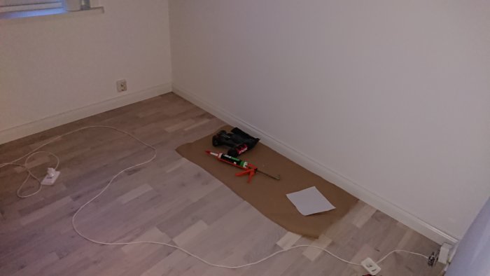 En tomrum med verktyg på golvet, kabeldragning pågår vid väggen i en pågående renovering.