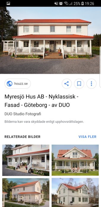 Ett stort vitmålat hus med rött tegeltak, veranda och vita staket, omgivet av grönska.