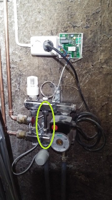 Golvvärmesystem med pump, rör, ventiler och termostater monterade på en källarvägg; mellanröret markerat med gult.