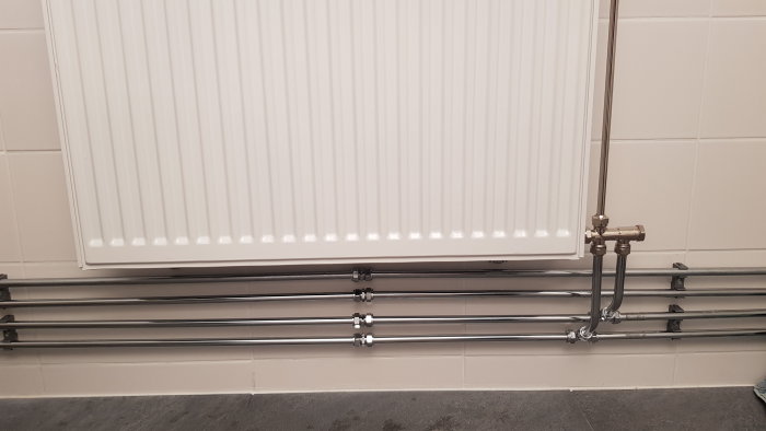 Radiator med kopplade rör och kopplingar längs en vägg, installation i tvättstuga.