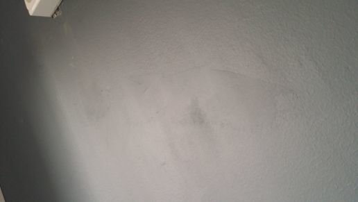 Ojämn väggstruktur med bredspackling och målningsfel i kök, synligt i sidoljus.