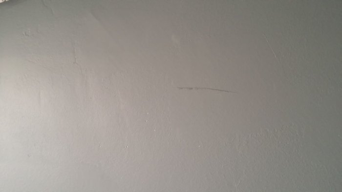 Ojämn bredspacklad och målad vägg med synlig struktur och repor i svagt ljus.