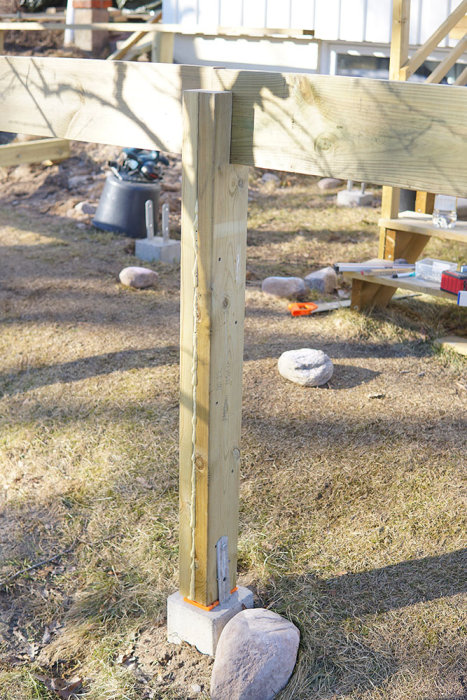 Nyuppsatt trästolpe med bärlina och verktyg synligt runt byggplatsen.