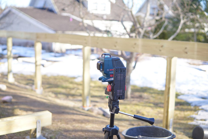 Laserverktyg i fokus med nyuppsatta trästolpar i bakgrunden, indikerar användning vid byggprojekt.