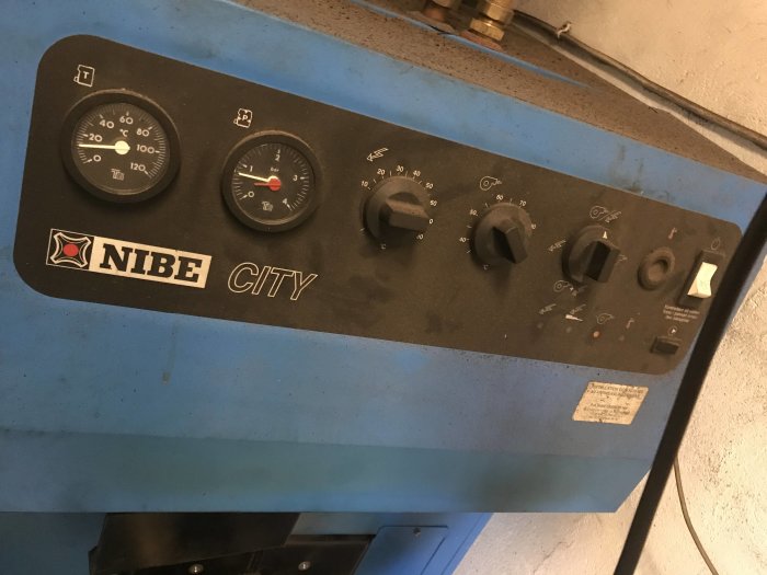 Kontrollpanel på en NIBE CITY panna med mätare, reglage och en väggströmbrytare.