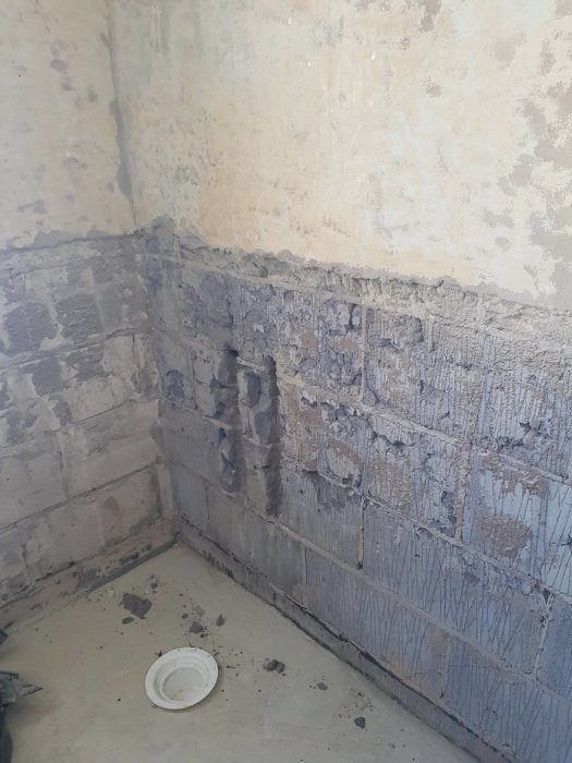 Renoveringsarbete i badrum med avlägsnat kakel och slipade väggar visande nivåskillnad och puts.