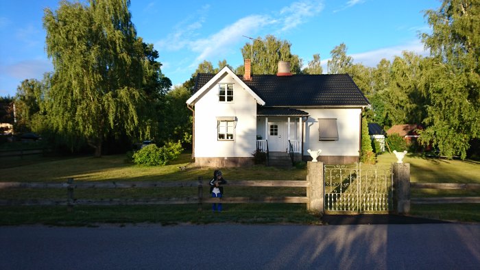 Vit villa med grön gräsmatta, träd och buskar lämplig för åkgräsklippning.