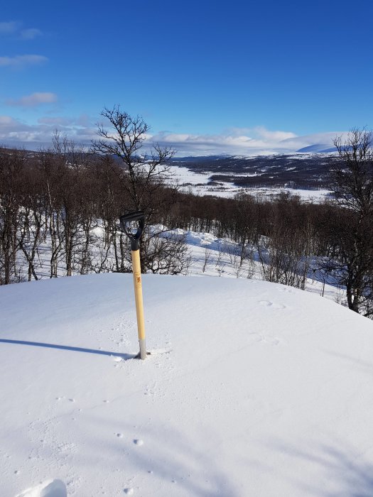 Snötäckt tak med en snöskyffel och utsikt över ett vinterlandskap med bergen i fjärran.