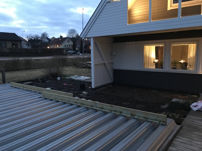 Avlägsnad trätrall intill ett hus visar en tom yta redo för grävningsarbete i skymningen.