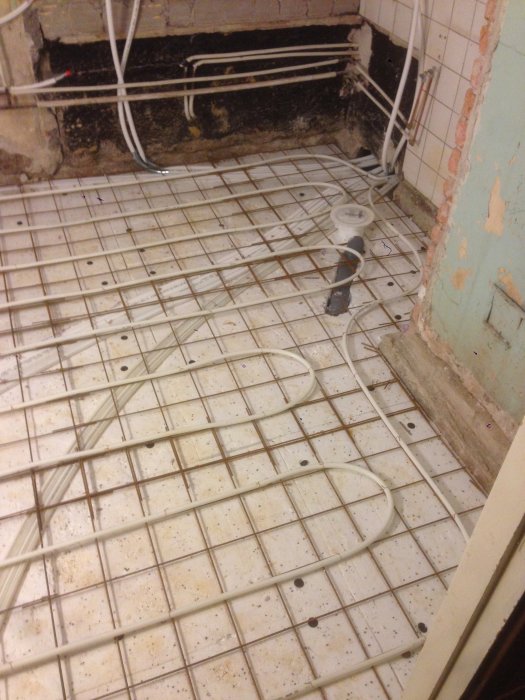 Armeringsnät och golvvärmerör på ett badrumsgolv under renovering.