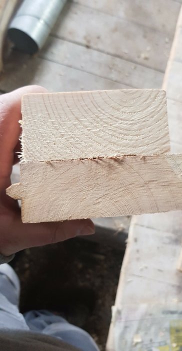 En hand håller två trästycken för att jämföra gammalt och nytt virke med synliga sågspår och träfibrer.