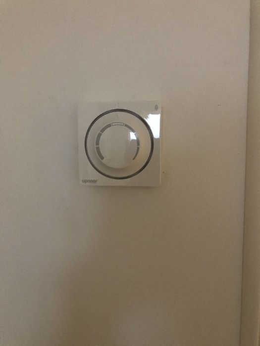 Väggmonterad termostat med vridreglage från Uponor för justering av rumstemperatur.