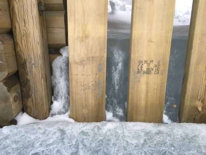 Träväggar av vågskydd på brygga med snö och is, tecken på hållbarhet genom vintern.