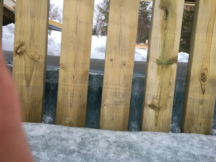 Trävågskydd vid en brygga med snö i bakgrunden.