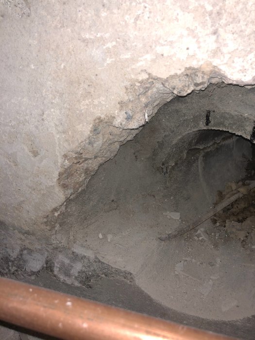 Delvis synligt mörkgrått betongrör med ojämnt putsad vägg, möjliga byggmaterial från Skanska.