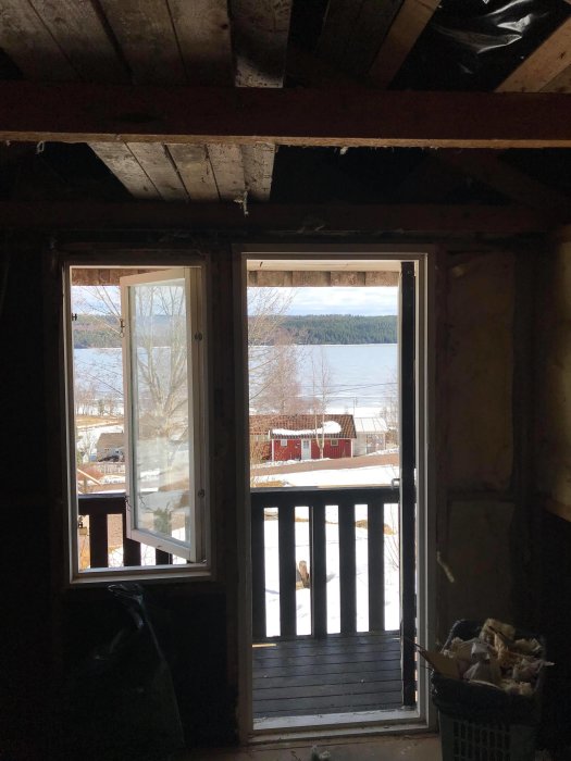 Utsikt från under renovering gäststuga med synlig isolering och snöig utsikt genom dörröppningen.