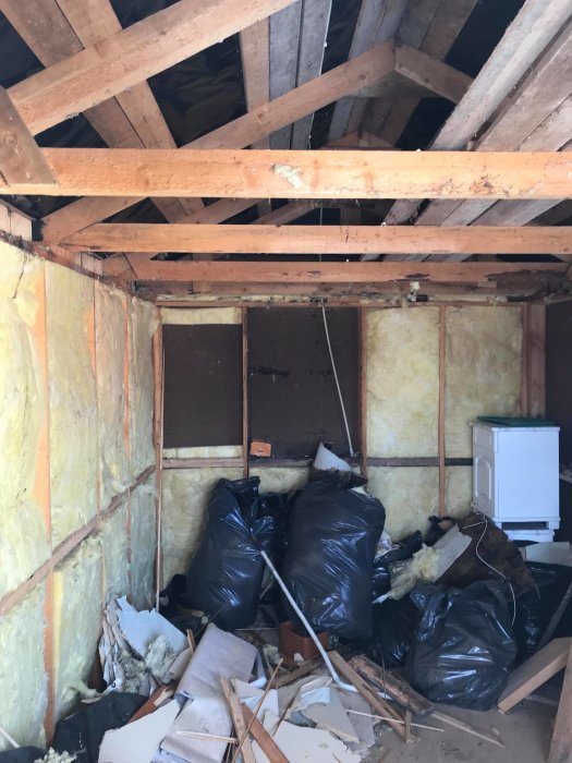 Renoveringsprojekt med exponerade väggreglar, uppbruten isolering och byggavfall på golvet.