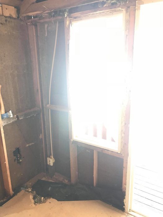 Renoveringsprojekt med exponerade väggreglar, skadad asfaltsboard och spånskivsgolv i ett urrivet rum.