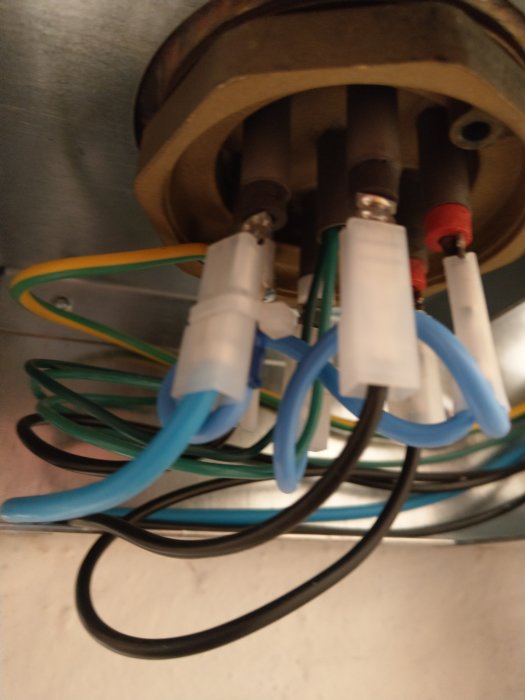 Anslutningar nära en elpatrons terminaler med olika färgade kablar och kopplingshus.