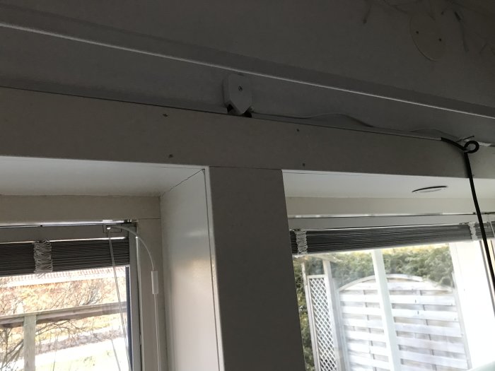 Omonterade gipsskivor nära ett fönster med rullgardin och synliga elledningar.