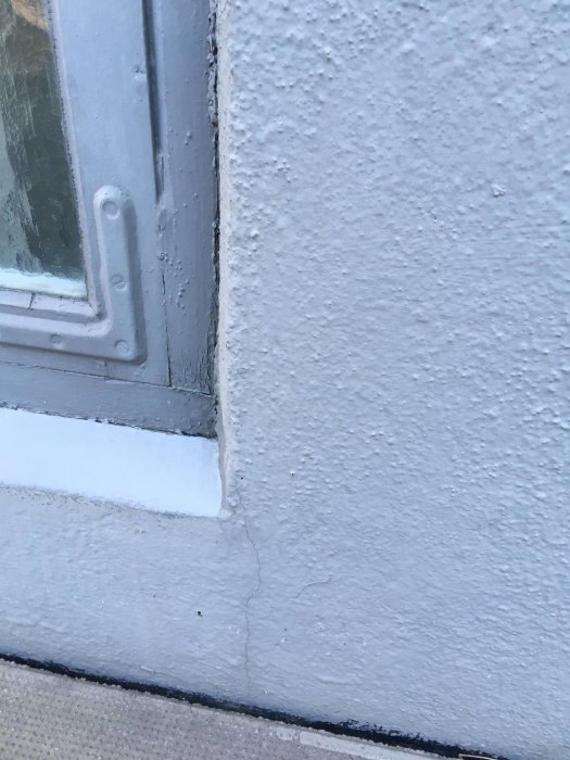 Sprickor i putsfasad nära fönstret på ett hus, skador efter kommunala arbeten.