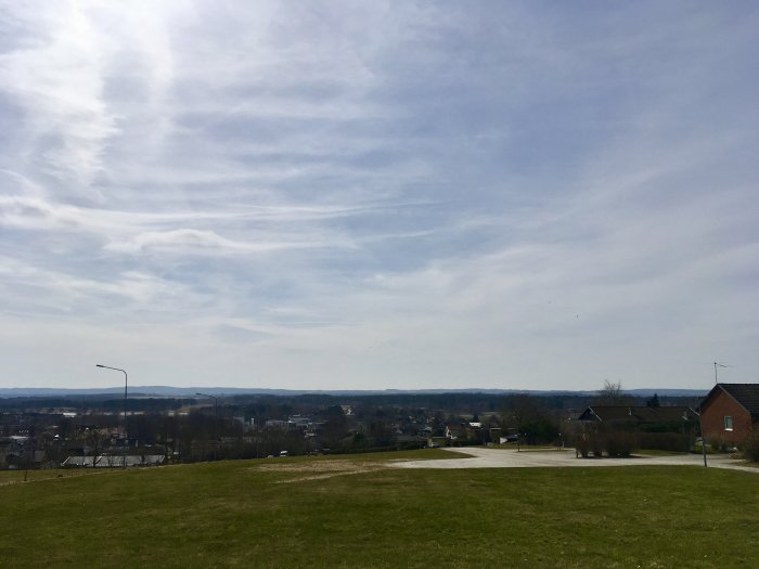 Utsikt över en solig park och stadslandskap i Skåne med blå himmel och lätta moln.