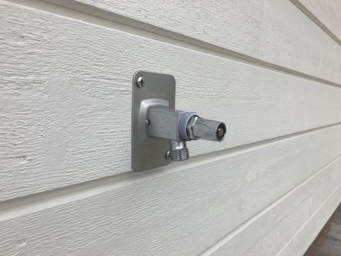 Monterad backventil på vit vägg med synliga skruvar och kopplingar.